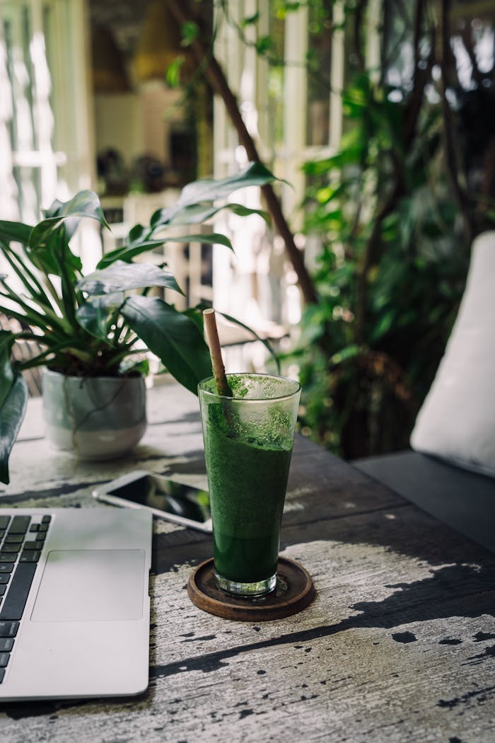 Refreshing green smoothie with bamboo straw amidst a cozy garden-style workspace.