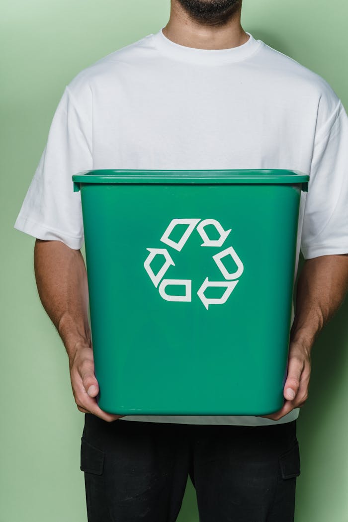 Adult male holding a green recycling bin against a green background, promoting sustainability.